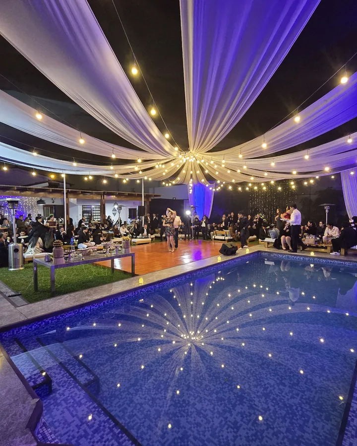 Salón de eventos de noche con telas blancas, luces cálidas y piscina iluminada