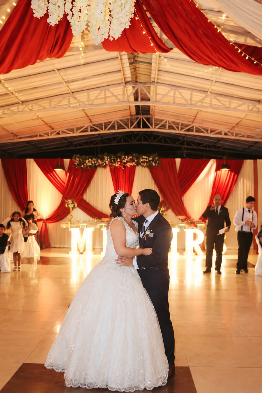 Novios besándose en su primer baile con decoración roja y blanca